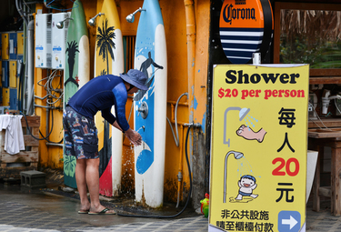 A surfer washing off sand and salt outside a surf shop along the main street parallel to Wushi, a popular surfing beach.