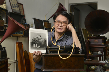 Record collector Dr Hsu Deng-fang holding a photograph of Thomas Edison listening to an Edison recording device as Dr Hsu listens to the vary same device amidst his collection of old gramophones locat...