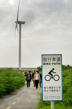 People walking along a bike path in the shadow of a massive wind turbine near the Taipower Company's Chang-Yi Switching Station, on Taiwan's windswept west coast.