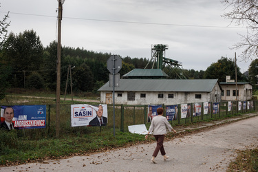 A woman walking to church for Sunday mass, passes a fence lined with election banners for PiS (Law & Justice, current ruling party).